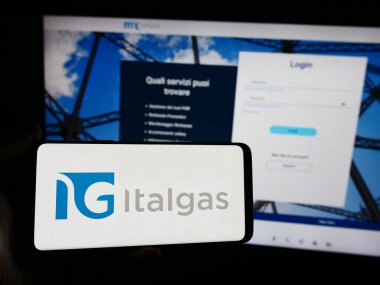 Stuttgart, Almanya - 08-16-2024: İtalyan doğalgaz dağıtım şirketi Italgas S.P.A. 'nın logosuna sahip akıllı telefon sahibi kişi web sitesinin önünde. Telefon ekranına odaklan.