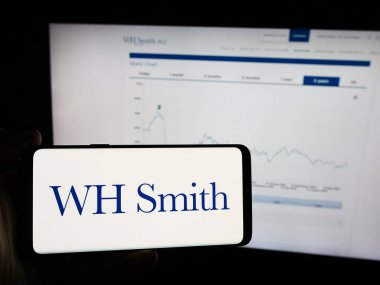 Stuttgart, Almanya - 08-16-2024: İngiliz perakende şirketi WH Smith plc 'in (WHSmith) logosuna sahip cep telefonu sahibi kişi iş sayfasının önünde. Telefon ekranına odaklan.