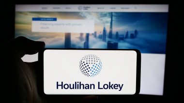 Stuttgart, Almanya - 08-16-2024: ABD 'li yatırım bankacılığı şirketi Houlihan Lokey Inc.' in logosuyla cep telefonu sahibi kişi iş sayfasının önünde. Telefon ekranına odaklan.
