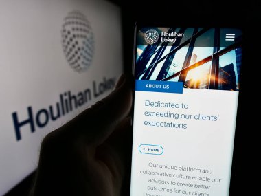 Stuttgart, Almanya - 08-16-2024: ABD 'li yatırım bankacılığı şirketi Houlihan Lokey Inc.' in web sayfası ile logo önünde cep telefonu tutan kişi. Telefon ekranının merkezine odaklan.
