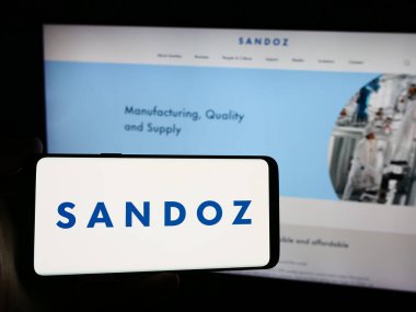 Stuttgart, Almanya - 08-16-2024: İsviçreli ilaç şirketi Sandoz Group AG 'nin logosuna sahip akıllı telefon sahibi kişi web sitesi önünde. Telefon ekranına odaklan.