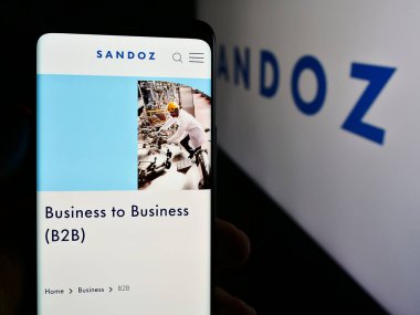 Stuttgart, Almanya - 08-16-2024: İsviçre ilaç şirketi Sandoz Group AG 'nin logo önündeki web sayfası ile cep telefonu tutan kişi. Telefon ekranının merkezine odaklan.
