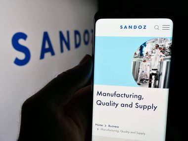 Stuttgart, Almanya - 08-16-2024: İsviçreli ilaç şirketi Sandoz Group AG 'nin web sitesiyle logo önünde cep telefonu tutan kişi. Telefon ekranının merkezine odaklan.