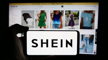 Stuttgart, Almanya - 08-16-2024: Moda e-ticaret şirketi Shein 'in logosuna sahip cep telefonu sahibi kişi iş sayfasının önünde. Telefon ekranına odaklan.