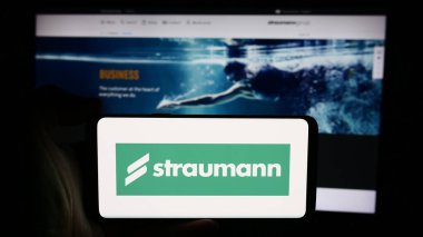 Stuttgart, Almanya - 08-16-2024: İsviçreli tıbbi cihaz şirketi Straumann Group 'un logosunun bulunduğu cep telefonu sahibi iş sayfası önünde bulunuyor. Telefon ekranına odaklan.