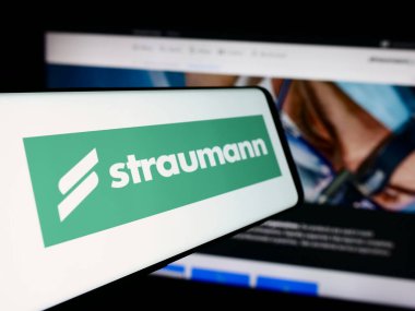 Stuttgart, Almanya - 08-16-2024: İsviçreli tıbbi cihaz şirketi Straumann Group 'un logosunun yer aldığı cep telefonu iş sitesi önünde. Telefon ekranının soluna odaklan.