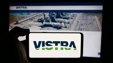 Stuttgart, Almanya - 08-16-2024: ABD 'li enerji şirketi Vistra Corp' un logosuyla cep telefonu sahibi kişi iş sayfasının önünde. Telefon ekranına odaklan.