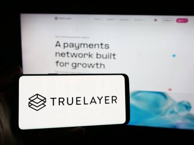 Stuttgart, Almanya - 08-18-2024: İngiliz bankacılık ödeme şirketi TrueLayer 'in logosuna sahip akıllı telefon sahibi kişi web sitesi önünde. Telefon ekranına odaklan.
