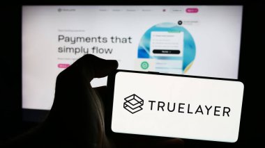 Stuttgart, Almanya - 08-18-2024: İngiliz bankacılık ödeme şirketi TrueLayer 'in logosuna sahip cep telefonu sahibi kişi iş sayfası önünde. Telefon ekranına odaklan.
