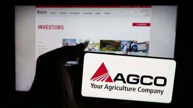 Stuttgart, Almanya - 08-18-2024: Web sitesi önünde üzerinde ABD tarım makineleri şirketi AGCO Corporation 'ın logosu bulunan akıllı telefon sahibi kişi. Telefon ekranına odaklan.