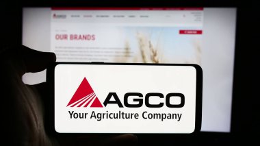 Stuttgart, Almanya - 08-18-2024: ABD tarım makineleri şirketi AGCO Corporation 'ın logosuyla cep telefonu sahibi kişi iş sayfası önünde. Telefon ekranına odaklan.