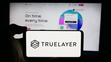 Stuttgart, Almanya - 08-18-2024: İngiliz bankacılık ödeme şirketi TrueLayer 'in logosuyla cep telefonu sahibi kişi iş sayfası önünde. Telefon ekranına odaklan.