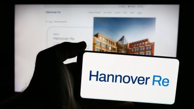 Stuttgart, Almanya - 08-18-2024: Alman sigorta şirketi Hannover Rueck SE 'nin logosuna sahip akıllı telefon sahibi kişi web sitesinin önünde. Telefon ekranına odaklan.