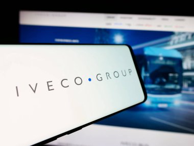 Stuttgart, Almanya - 08-18-2024: İtalyan ticari araç şirketi Iveco Group NV 'nin logosunu taşıyan cep telefonu, iş sitesinin önünde. Telefon ekranının merkez soluna odaklan.