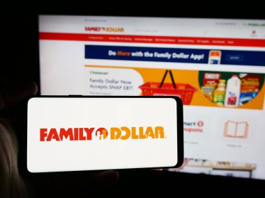 Stuttgart, Almanya - 08-19-2024: İnternet sitesi önünde üzerinde ABD 'li çeşitli mağaza şirketi Family Dollar Stores Inc.' in logosu bulunan kişi. Telefon ekranına odaklan.