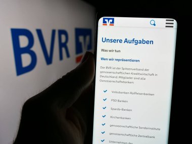 Stuttgart, Almanya - 08-19-2024: Logolu Ulusal Alman Kooperatif Bankalar Birliği (BVR) web sayfası ile cep telefonu tutan kişi. Telefon ekranının merkezine odaklan.