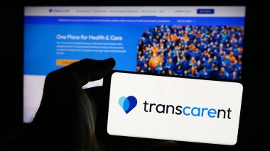 Stuttgart, Almanya - 08-19-2024: Amerikan sağlık şirketi Transcarent Inc. 'in logosuna sahip cep telefonu sahibi kişi iş sayfasının önünde. Telefon ekranına odaklan.