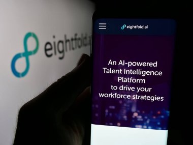 Stuttgart, Germany - 08-19-2024: Person holding cellphone with webpage of US talent intelligence company Eightfold AI Inc. in front of logo. Focus on center of phone display. clipart