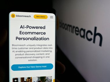 Stuttgart, Germany - 08-19-2024: Person holding smartphone with web page of US e-commerce platform company Bloomreach Inc. in front of logo. Focus on center of phone display. clipart