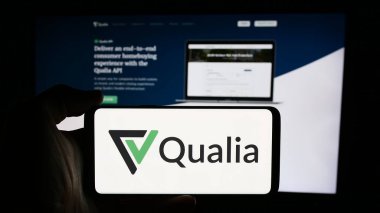 Stuttgart, Almanya - 08-19-2024: ABD 'li emlak platformu şirketi Qualia Labs Inc.' in logosuyla cep telefonu sahibi kişi iş sayfasının önünde. Telefon ekranına odaklan.