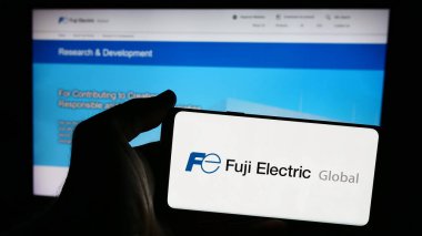 Stuttgart, Almanya - 08-20-2024: Japon şirketi Fuji Electric Co. Ltd. nin logosuna sahip akıllı telefon sahibi kişi web sitesinin önünde. Telefon ekranına odaklan.