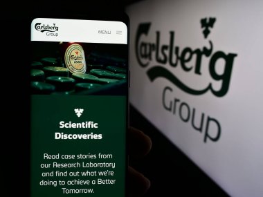 Stuttgart, Almanya - 08-20-2024: Danimarkalı bira şirketi Carlsberg AS 'in web sayfası ile akıllı telefon taşıyan kişi iş logosu önünde. Telefon ekranının merkezine odaklan.
