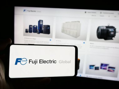 Stuttgart, Almanya - 08-20-2024: Japon firması Fuji Electric Co. Ltd. nin logosuyla cep telefonu tutan kişi iş sayfasının önünde. Telefon ekranına odaklan.