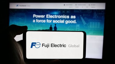 Stuttgart, Almanya - 08-20-2024: Japon şirketi Fuji Electric Co. Ltd. nin logosuyla cep telefonu tutan kişi iş sayfasının önünde. Telefon ekranına odaklan.