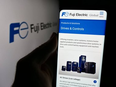 Stuttgart, Almanya - 08-20-2024: Japon firması Fuji Electric Co. Ltd. nin internet sayfası ile birlikte iş logosu önünde cep telefonu tutan kişi. Telefon ekranının merkezine odaklan.