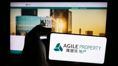 Stuttgart, Almanya - 08-20-2024: Çinli şirket Agile Property Holding Limited 'in logosuna sahip cep telefonu sahibi kişi iş sayfasının önünde. Telefon ekranına odaklan.