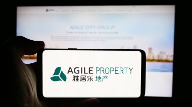 Stuttgart, Almanya - 08-20-2024: Çinli şirket Agile Property Holding Limited 'in logosuna sahip cep telefonu sahibi kişi iş sayfasının önünde. Telefon ekranına odaklan.