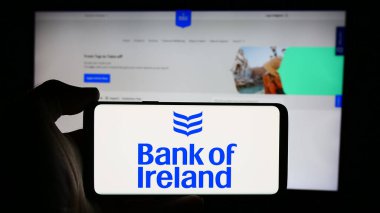Stuttgart, Almanya - 08-20-2024: İrlandalı finans şirketi Bank of Ireland Group plc 'in logosuyla cep telefonu tutan kişi iş sayfasının önünde. Telefon ekranına odaklan.