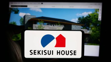 Stuttgart, Almanya - 08-20-2024: Japon ev yapımı şirketi Sekisui House Ltd. 'nin logosuyla cep telefonu tutan kişi iş sayfasının önünde. Telefon ekranına odaklan.