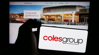 Stuttgart, Germany - 08-20-2024: Person holding mobile phone with logo of Australian retail company Coles Group Limited in front of business web page. Focus on phone display. clipart