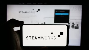 Stuttgart, Germany - 08-21-2024: Person holding cellphone with logo of application programming interface Steamworks (Steam) in front of business webpage. Focus on phone display. clipart