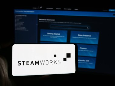 Stuttgart, Almanya - 08-21-2024: Web sayfasının önünde uygulama programlama arayüzü logosu (Steam) bulunan cep telefonu sahibi kişi. Telefon ekranına odaklan.