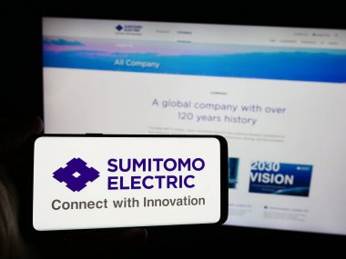 Stuttgart, Almanya - 08-21-2024: Japon şirketi Sumitomo Electric Industries Ltd. 'nin logosuna sahip akıllı telefon sahibi kişi web sitesinin önünde. Telefon ekranına odaklan.