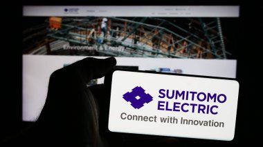 Stuttgart, Almanya - 08-21-2024: Japon şirketi Sumitomo Electric Industries Ltd. 'nin logosuna sahip cep telefonu sahibi kişi iş sayfasının önünde. Telefon ekranına odaklan.