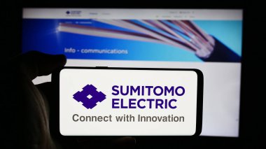 Stuttgart, Almanya - 08-21-2024: Japon şirketi Sumitomo Electric Industries Ltd. 'nin logosuyla cep telefonu tutan kişi iş sayfasının önünde. Telefon ekranına odaklan.