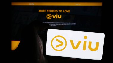 Stuttgart, Almanya - 08-21-2024: İş sayfası önünde Hong Kong yayın hizmeti şirketi Viu 'nun logosuyla cep telefonu tutan kişi. Telefon ekranına odaklan.