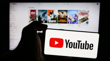 Stuttgart, Almanya - 08-21-2024: İnternet sayfası önünde Amerikan çevrimiçi video paylaşım platformu YouTube logosu olan cep telefonu sahibi kişi. Telefon ekranına odaklan.