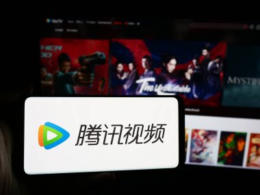 Stuttgart, Germany - 08-22-2024: Person holding smartphone with logo of Chinese video streaming service Tencent Video (WeTV) in front of website. Focus on phone display. clipart