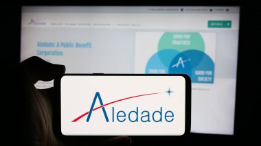 Stuttgart, Almanya - 08-22-2024: ABD 'li birincil bakım ağı şirketi Aledade Inc.' in logosuyla cep telefonu sahibi kişi iş sayfasının önünde. Telefon ekranına odaklan.