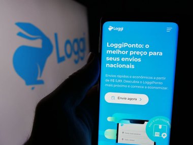 Stuttgart, Almanya - 08-26-2024: Brezilyalı yazılım şirketi Loggi Tecnologia Ltda 'nın internet sayfası ile cep telefonu tutan kişi. Logonun önünde. Telefon ekranının merkezine odaklan.