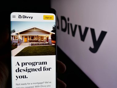 Stuttgart, Almanya - 08-26-2024: ABD 'li emlak şirketi Divvy Homes Inc.' in internet sayfası ile akıllı telefon sahibi kişi iş logosu önünde. Telefon ekranının merkezine odaklan.