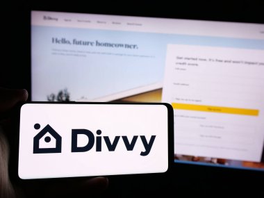 Stuttgart, Almanya - 08-26-2024: Üzerinde ABD 'li emlak şirketi Divvy Homes Inc.' in logosu bulunan cep telefonu sahibi kişi iş sayfasının önünde. Telefon ekranına odaklan.