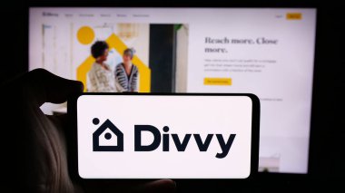 Stuttgart, Almanya - 08-26-2024: Üzerinde Amerikan emlak şirketi Divvy Homes Inc. 'in logosu bulunan cep telefonu sahibi kişi iş sayfasının önünde. Telefon ekranına odaklan.