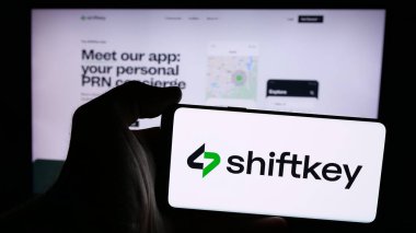 Stuttgart, Germany - 08-27-2024: Person holding smartphone with logo of US healthcare platform company ShiftKey LLC in front of website. Focus on phone display. clipart