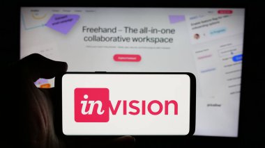 Stuttgart, Germany - 08-28-2024: Person holding cellphone with logo of US collaboration software company InVisionApp Inc. in front of business webpage. Focus on phone display. clipart