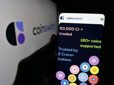 Stuttgart, Germany - 09-27-2024: Person holding cellphone with webpage of Indian crypto platform company CoinSwitch on screen in front of logo. Focus on center of phone display. clipart